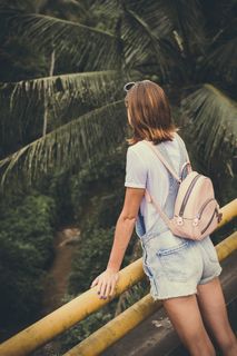 白天，一名身穿工装裤的妇女站在一条黄色金属栏杆旁，俯瞰着一条长满椰子树的贝洛河