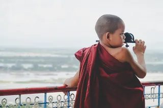 白天，身穿红色服装的男孩靠在蓝色和红色金属栏杆上