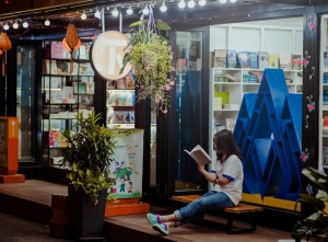 女人坐在长椅上，在商店前看书