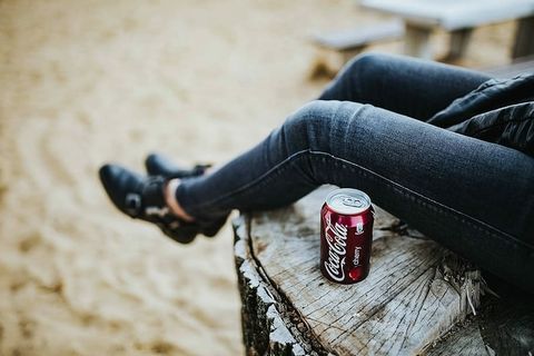 美丽的金发女人在海滩边的树桩上拿着一罐可乐放松