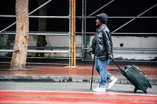 穿着黑色皮夹克和蓝色牛仔裤的徒步男子，手拿行李袋