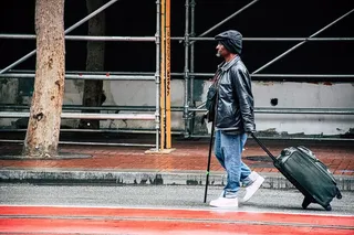 穿着黑色皮夹克和蓝色牛仔裤的徒步男子，手拿行李袋