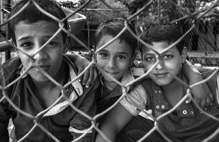 铁栅栏旁三个男孩的灰度照片