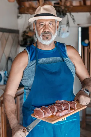 穿着蓝色围裙的男子拿着刀和切肉板