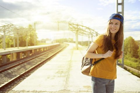 身着橙色T恤和蓝色按扣帽的微笑女子，背着背包