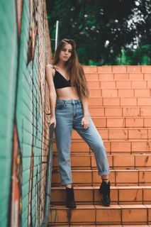 一名身穿黑色胸罩和牛仔服、靠在棕色墙上的妇女