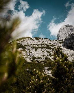 灰色和绿色的岩石山在白色和蓝色的多云天空下