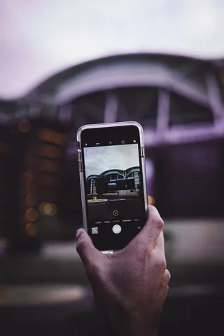 白天用手机拍摄灰色建筑照片的人