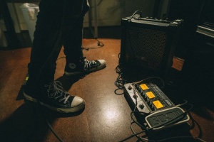 站在吉他扩音器和吉他踏板变形旁边的男子