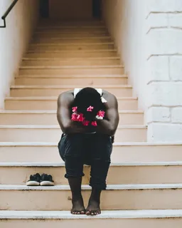 穿着白色背心和黑色牛仔裤坐在楼梯上的男子