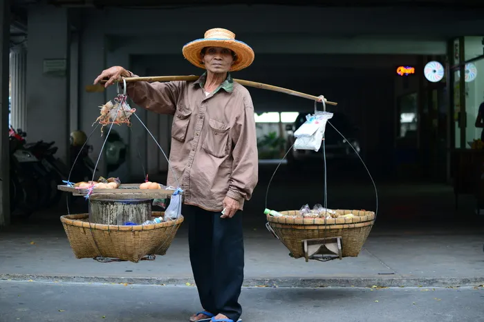 身穿棕色夹克的男子肩上的木杆上挂着两个篮子