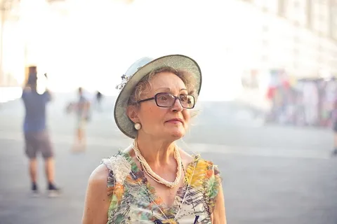 特写镜头:身穿蜡笔色上衣、戴太阳帽、戴眼镜在街上行走的老年妇女 特写镜头:身穿蜡笔色上衣、戴太阳帽、戴眼镜在街上行走的老年妇女