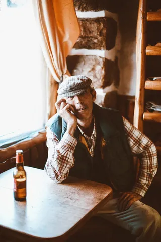 身穿红白格子衬衫和黑色背心的男子坐在棕色木桌旁