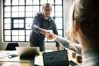 坐在桌子旁边的女人和对面搁浅的男人握手