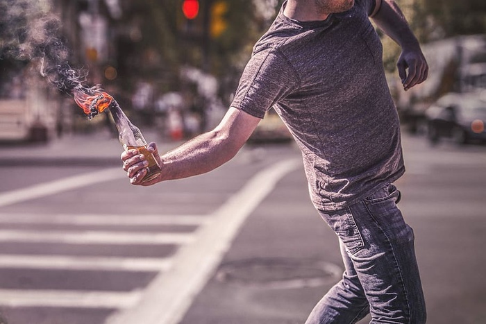 一名身穿灰色衬衫的男子在街上举着燃烧的燃烧弹