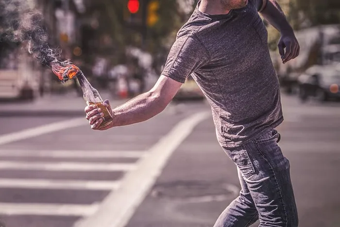 一名身穿灰色衬衫的男子在街上举着燃烧的燃烧弹