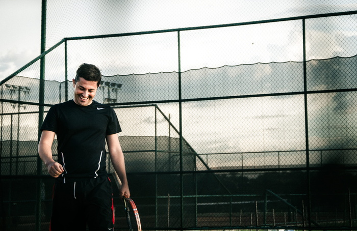 男子身穿黑色Nike Dri-fit衬衫，手持网球拍