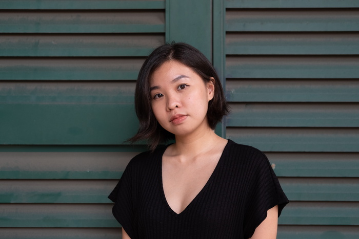 身穿黑色低垂领口连衣裙的女子站在绿色墙面前