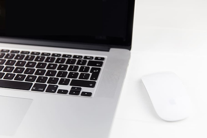 苹果Macbook Pro笔记本电脑和魔法鼠标位于极简主义的纯白色木桌上