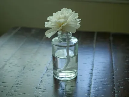 精油扩散器，顶部有一朵花，坐在一张木桌上。