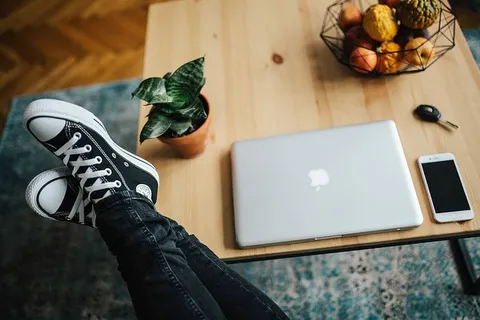 穿着破牛仔裤和黑色运动鞋的女人，在木桌上放着一台银色笔记本电脑