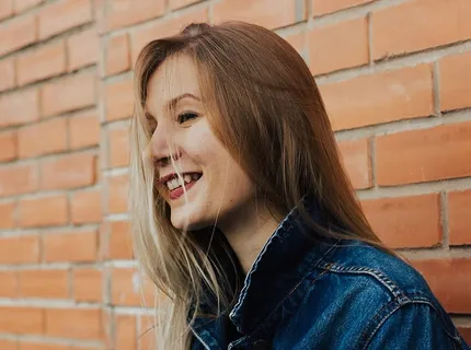 一名身穿蓝色牛仔夹克的女子倚在砖墙上