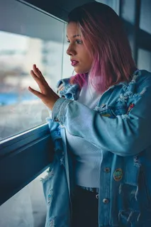 粉红色头发的女人站在窗边的照片 粉红色头发的女人站在窗边的照片