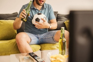 年轻人在电视上看足球，在家里喝啤酒