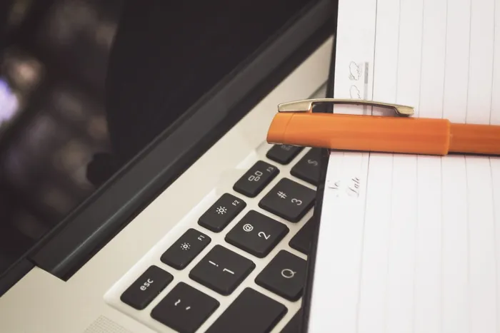 在MacBook键盘上放置一支橙色钢笔的笔记皮记事本