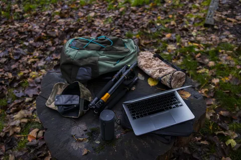 树桩上的银色笔记本电脑、包和三脚架