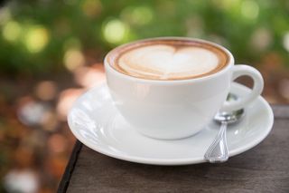 微距摄影中带碟子的白色陶瓷杯上的拿铁咖啡