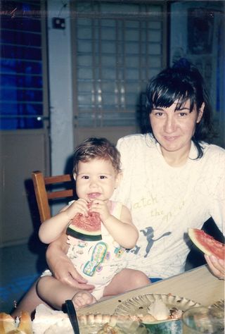 一位身穿白衬衫的妇女抱着一个正在吃西瓜的蹒跚学步的孩子