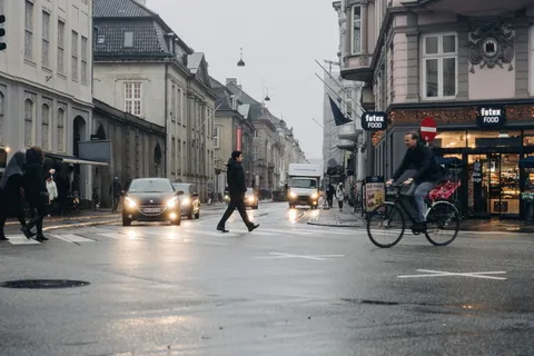 白天穿黑色夹克穿过马路的男子