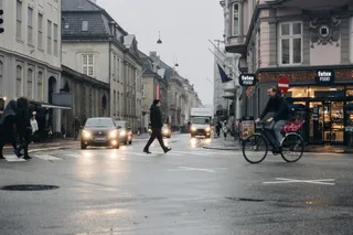 白天穿黑色夹克穿过马路的男子