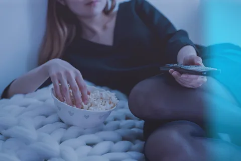 白色床上的女人一边吃爆米花一边拿着遥控器 白色床上的女人一边吃爆米花一边拿着遥控器