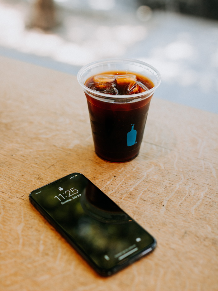 黑色iPhone 7旁边是一个透明的一次性杯子，里面装满了饮料和冰块