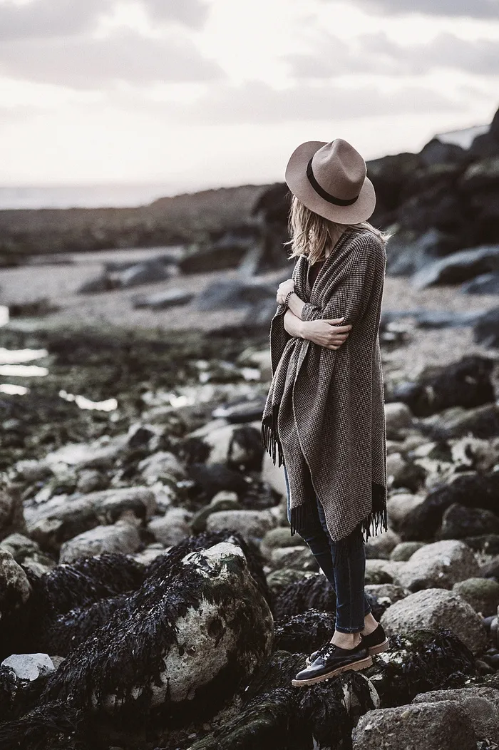 穿着垂褶外套的女人站在面向岩石的山上