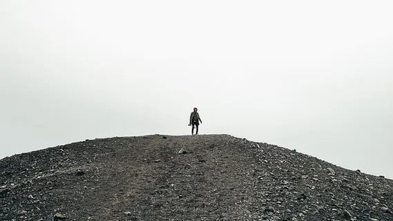 一个携带相机的徒步旅行者站在一座砾石小山上 一个携带相机的徒步旅行者站在一座砾石小山上