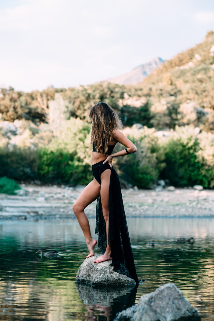 白天，一名身穿黑色短上衣的妇女站在水体上的灰色石头旁