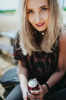 美丽的金发女人在海滩边的树桩上拿着一罐可乐放松