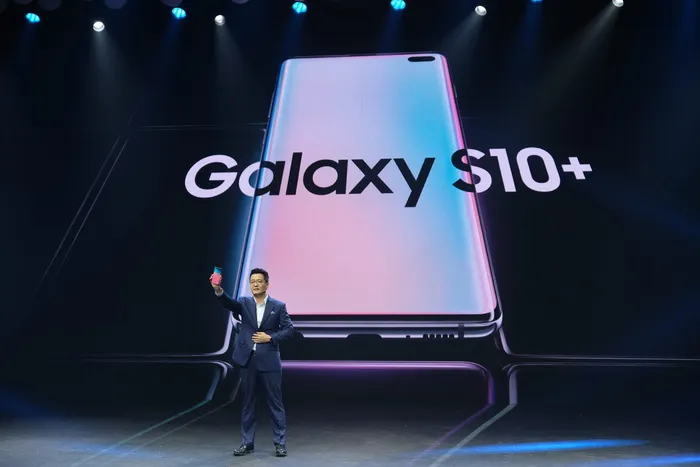 站在投影仪屏幕旁的男子，黑色三星Galaxy S10+文字