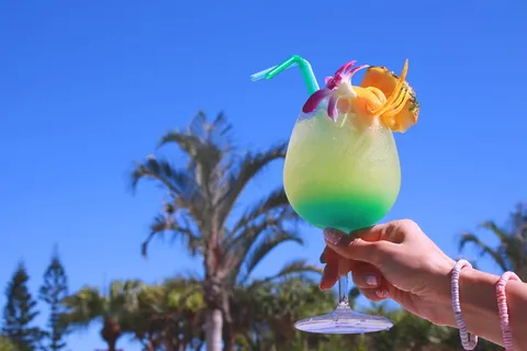 在晴朗的蓝天下,一个人拿着黄色和青色液体填充的脚踏玻璃 在晴朗的蓝天下,一个人拿着黄色和青色液体填充的脚踏玻璃