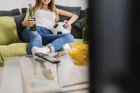 非常兴奋的年轻女子在家里看电视上的足球比赛。 非常兴奋的年轻女子在家里看电视上的足球比赛。