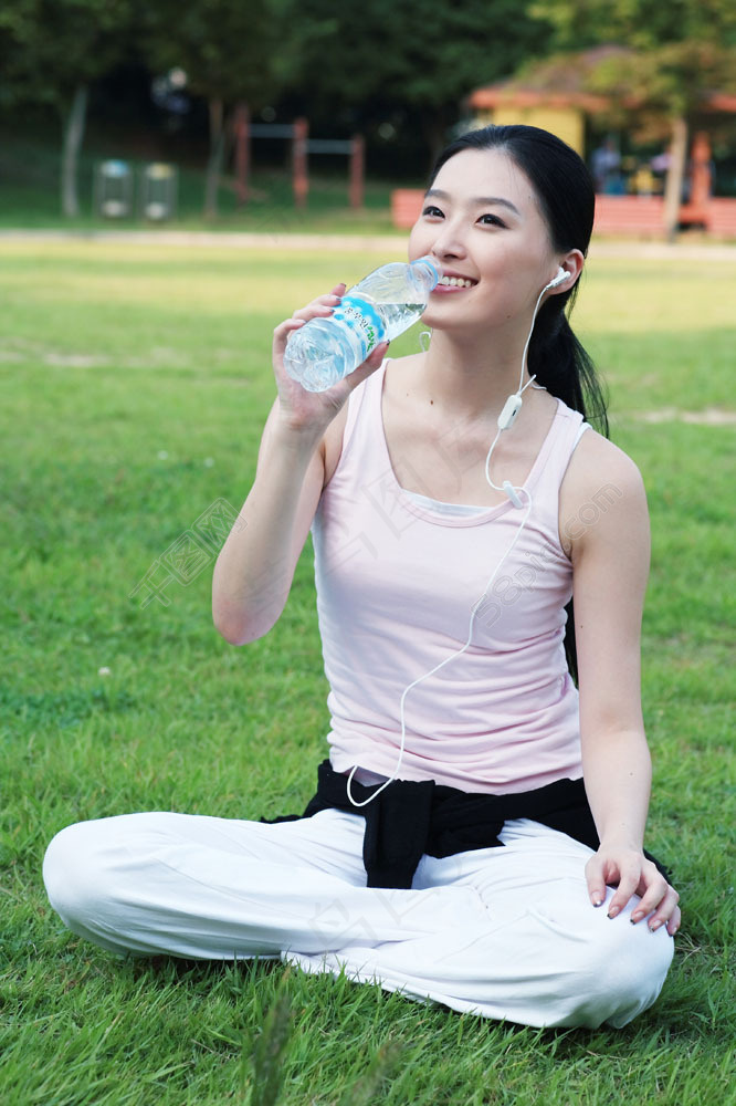 草地上喝水听音乐的女孩图片图片