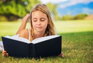 趴在草地上看书的外国小女孩图片