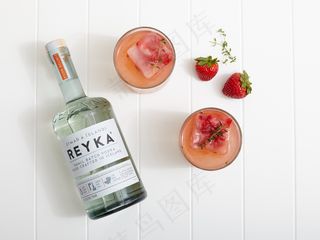 草莓伏特加粉碎鸡尾酒在旁边一瓶和两个草莓与百里香的白色桌子上的两个杯子