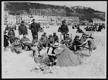 英国，法国和美国士兵在沙滩上坐着W.A.A.C.s，看着法国小伙子们建造沙堡