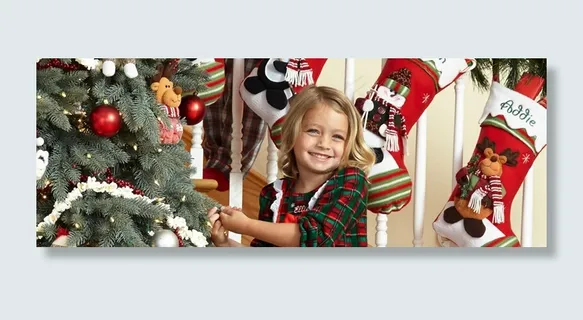 微笑在楼梯栏杆与个性化的长袜和它与装饰品和花环的松树圣诞树上的小女孩