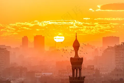 日落在从Al Azhar庭院的开罗。在背景中，金字塔位于两座建筑物的后面。前面的尖塔周围有鸟。