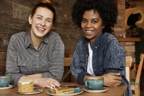 两个快乐的非洲和高加索女同性恋在舒适的咖啡馆享受午餐时光 两个快乐的非洲和高加索女同性恋在舒适的咖啡馆享受午餐时光